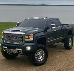 a large black truck parked on top of a dirt road next to a body of water