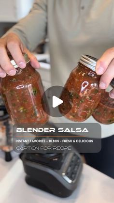 two hands holding jars filled with food on top of a counter next to a blender