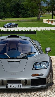 a silver sports car parked on top of a gravel road next to a lush green field