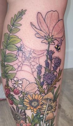 a woman's thigh with flowers and leaves on it, as well as a bee