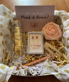 a box with some gold and white items in it, including a card that says will you be my maid of honor?