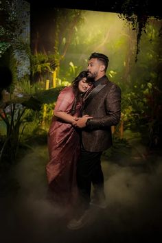 a man and woman standing next to each other in front of a forest scene with fog