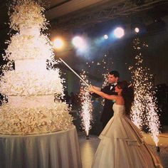 a newly married couple standing next to a wedding cake with sparklers in the air