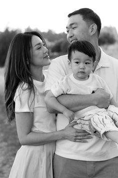 a man and woman holding a baby while standing next to each other in a field