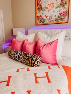 a bed with pink and orange pillows on top of it next to a framed painting