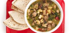 a bowl of soup with tortillas on a red plate next to some pita bread