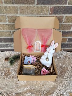 an open cardboard box with items inside on a lace table cloth covered tablecloth and brick wall behind it