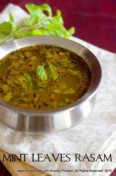 a metal bowl filled with soup sitting on top of a wooden cutting board next to a green leafy plant