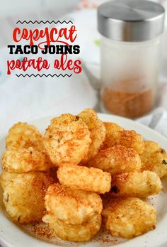 some tater tots are on a white plate next to a jar of seasoning