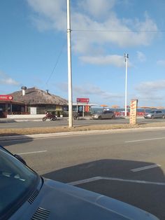 cars are parked on the side of the road in front of a building with a thatched roof