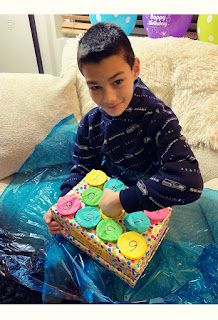 a young boy sitting on a couch holding a box of decorated birthday cake with frosting and sprinkles