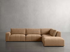 a beige couch sitting on top of a floor next to a gray wall with no one in it