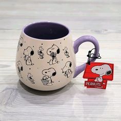 a purple and white coffee mug with peanuts on it, next to a tag that says peanuts