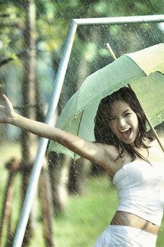 a woman holding an umbrella in the rain with her arms out and smiling at the camera