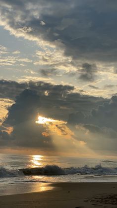 the sun is setting over the ocean with clouds in the sky and waves crashing on the beach