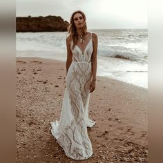 a woman standing on top of a beach next to the ocean wearing a white dress