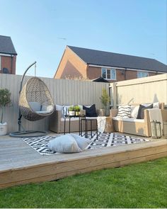 an outdoor living area with wooden decking and wicker furniture on the grass in front of a house