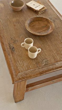 a wooden table topped with two cups and saucers next to a book on top of it