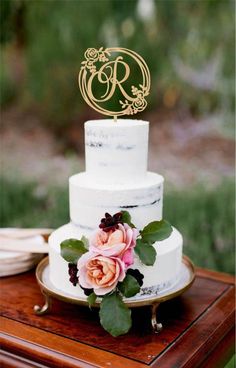 a three tiered white cake with pink flowers on top and gold lettering that says madison stationers