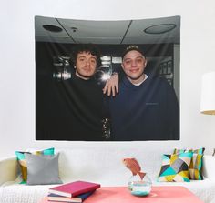 two men standing next to each other in front of a wall hanging on the wall