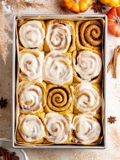 cinnamon rolls with icing in a pan surrounded by pumpkins and other autumn decorations