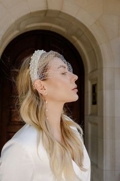 a woman wearing a veil with pearls on her head is standing in front of a door