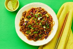 a white bowl filled with noodles and meat next to chopsticks on a green surface