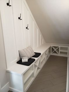 a white bench sitting under a slanted ceiling next to a wall with hooks on it