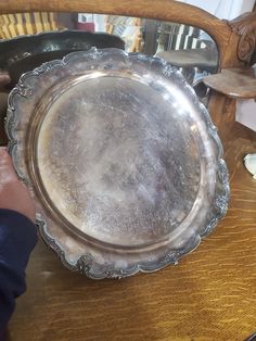 a silver plate sitting on top of a wooden table next to a person's hand