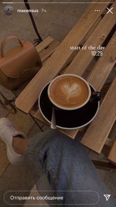 a cup of coffee sitting on top of a wooden table next to a handbag