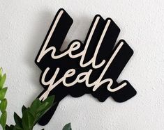 a black and white sign that says hell yeah on the side of a wall next to a potted plant