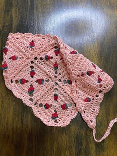 a pink crocheted hat sitting on top of a wooden table next to a string