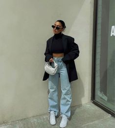 a woman standing in front of a building wearing high waist jeans and black blazer