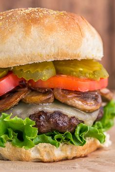 a hamburger with pickles, tomatoes, onions and cheese on it sitting on a wooden surface