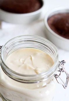 a jar filled with cream sitting on top of a counter next to two bowls full of chocolate pudding