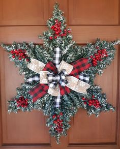 a christmas wreath hanging on the front door with red and white bows, pine cones and plaid ribbon