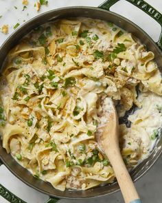 a skillet filled with pasta and peas on top of a table next to a wooden spoon