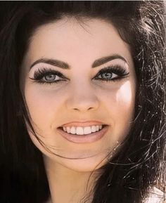 a woman with long black hair and blue eyes smiles at the camera while wearing makeup