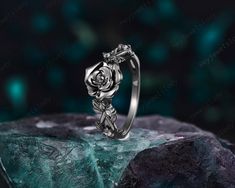 a silver rose ring sitting on top of a rock with green rocks in the background