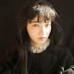 a woman with long dark hair wearing a black sweater and white collared shirt looking at the camera