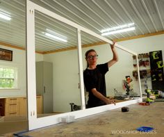 a woman standing in front of a mirror holding up a piece of wood to the side