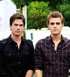 two young men standing next to each other in front of a white truck and trees