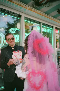 a man and woman standing next to each other in front of a store window holding a cake