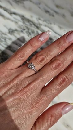 a woman's hand with pink and white nail polish holding a ring on her finger