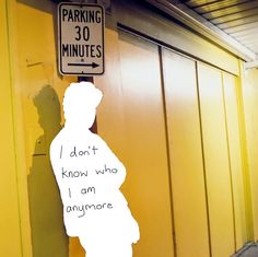 a man standing next to a parking sign on the side of a yellow building with writing on it