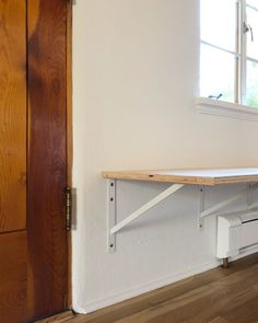 an empty room with a wooden door and white shelf on the wall next to a window