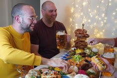 three men sitting at a table with food and drinks