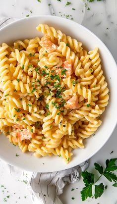 pasta with salmon and parsley in a white bowl on a marble table top next to fresh parsley