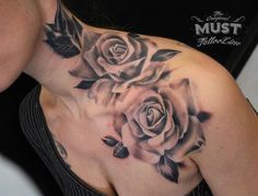 a woman's chest with roses and leaves tattooed on her shoulder, in black and white