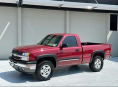 a red pick up truck parked in front of a white garage door on a sunny day